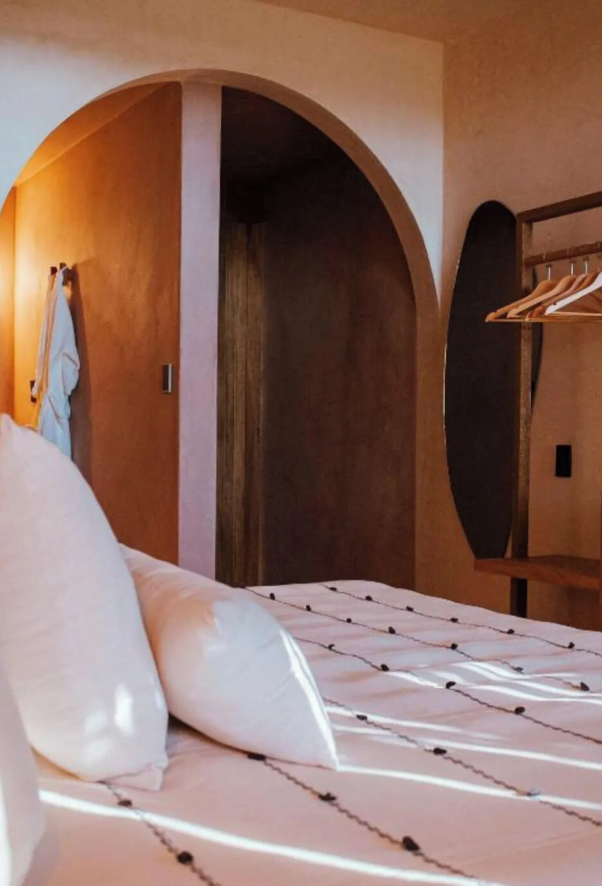 Balcony Atelier: cama con cojines blancos y un arco de chukum hacia el baño, con perchero y espejo ovalado