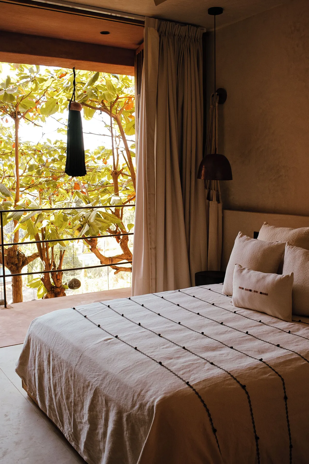 Balcony Atelier: cama frente al balcón abierto, con cortina de lino y árboles del jardín al otro lado del barandal