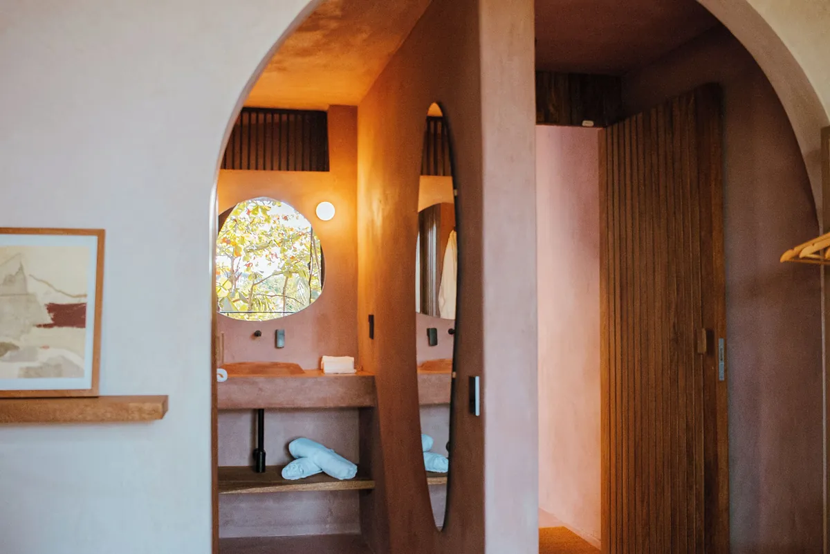 Balcony Atelier: arco hacia el lavabo de chukum con ventana circular y espejo ovalado, junto a una puerta de madera