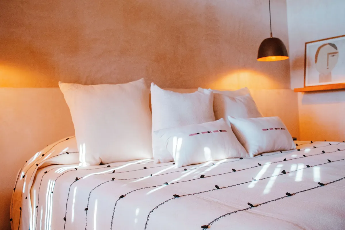 Balcony Atelier: cama con colcha de rayas y cojines blancos bajo una lámpara colgante, junto a un cuadro de líneas