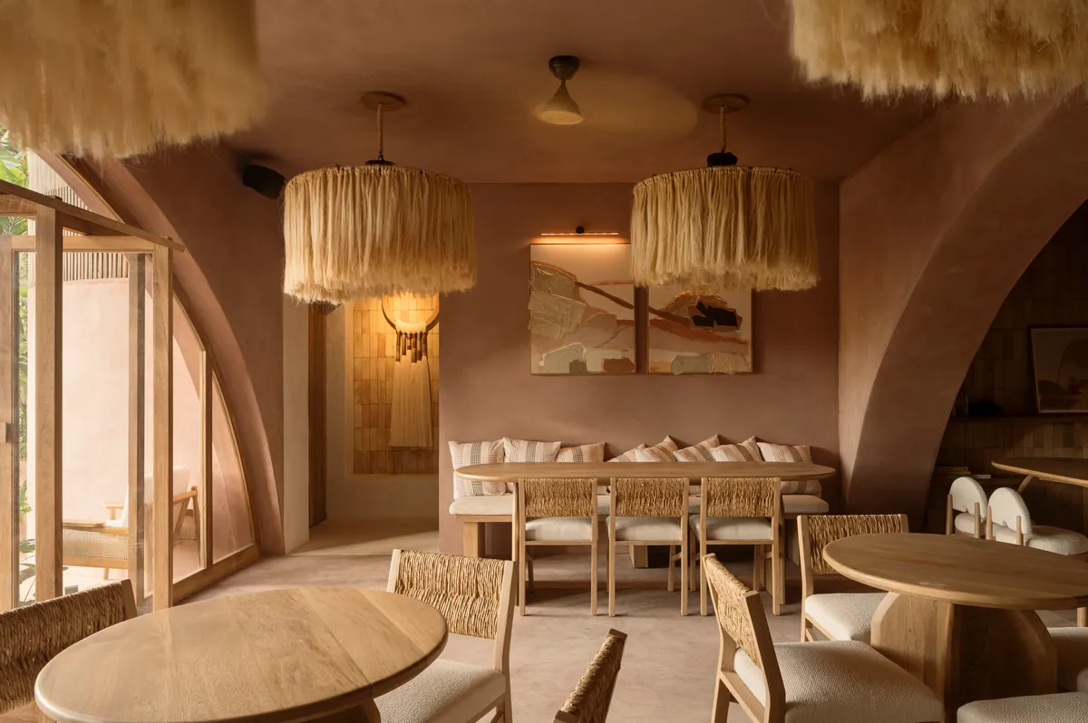 Comedor con muros y arcos de chukum rosado, lámparas de fibra natural, mesas de madera y sillas tejidas
