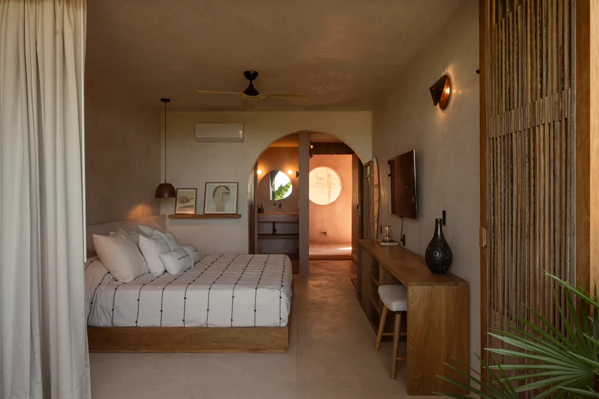 Grand Signature: cama de plataforma de madera, escritorio largo y un arco hacia el baño con espejo redondo y ventana circular