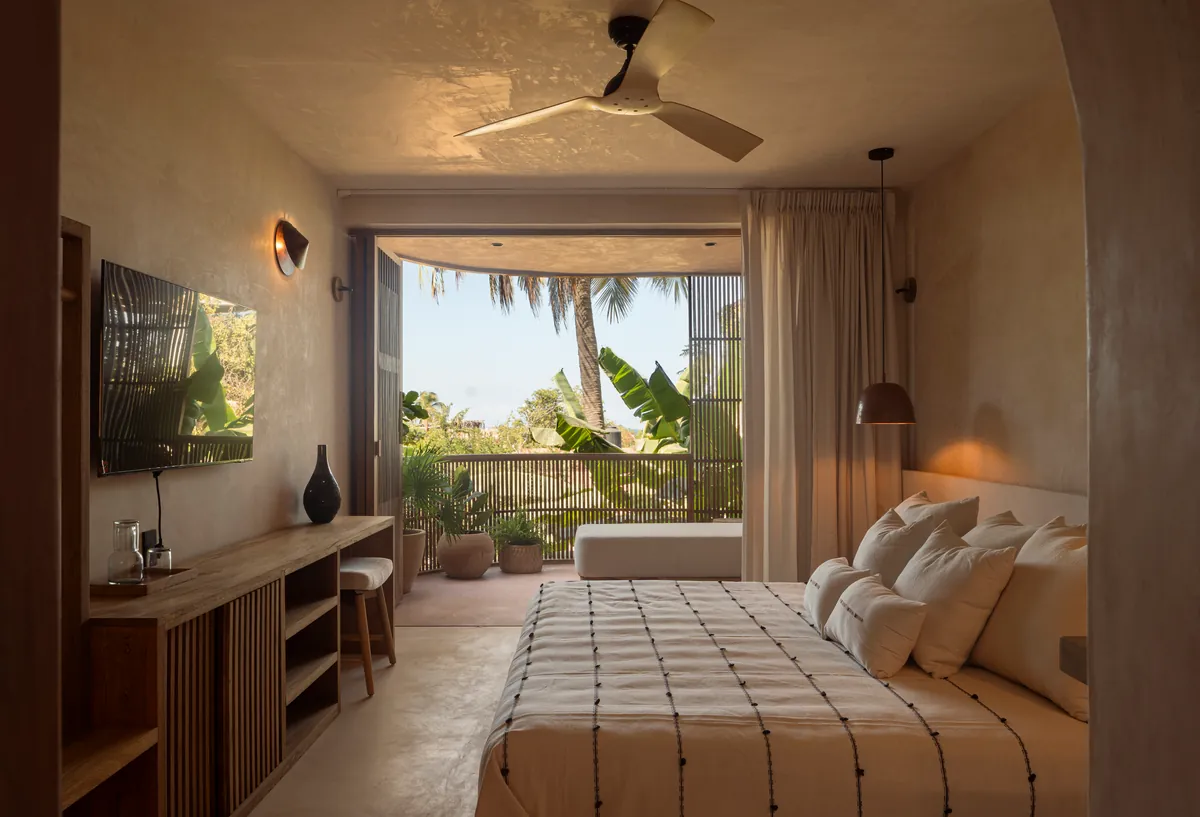 Grand Signature: cama amplia con colcha de rayas, mueble de madera y ventilador de techo; al fondo, la terraza con camastro y una palmera