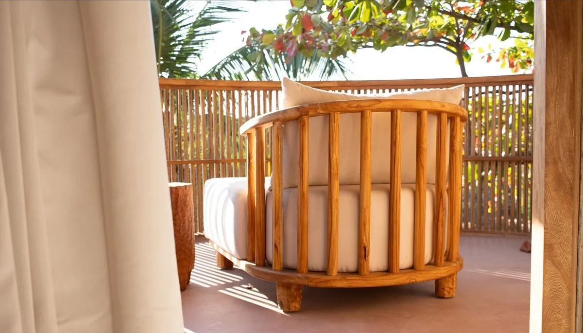 Pacific Terrace: sillón redondo de madera con cojines claros en la terraza, entre celosías de varas y vegetación