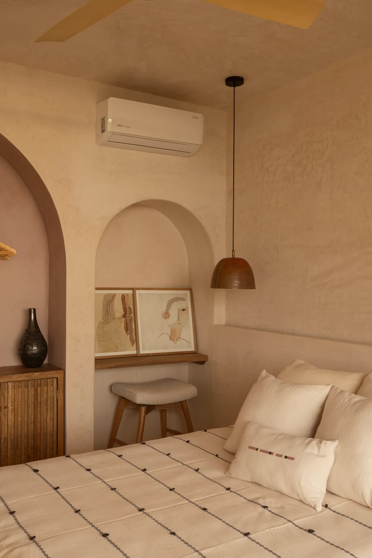 Pacific Terrace: nicho en arco con repisa de madera para escribir, banco tapizado y dos láminas junto a la cama, bajo una lámpara colgante color cobre