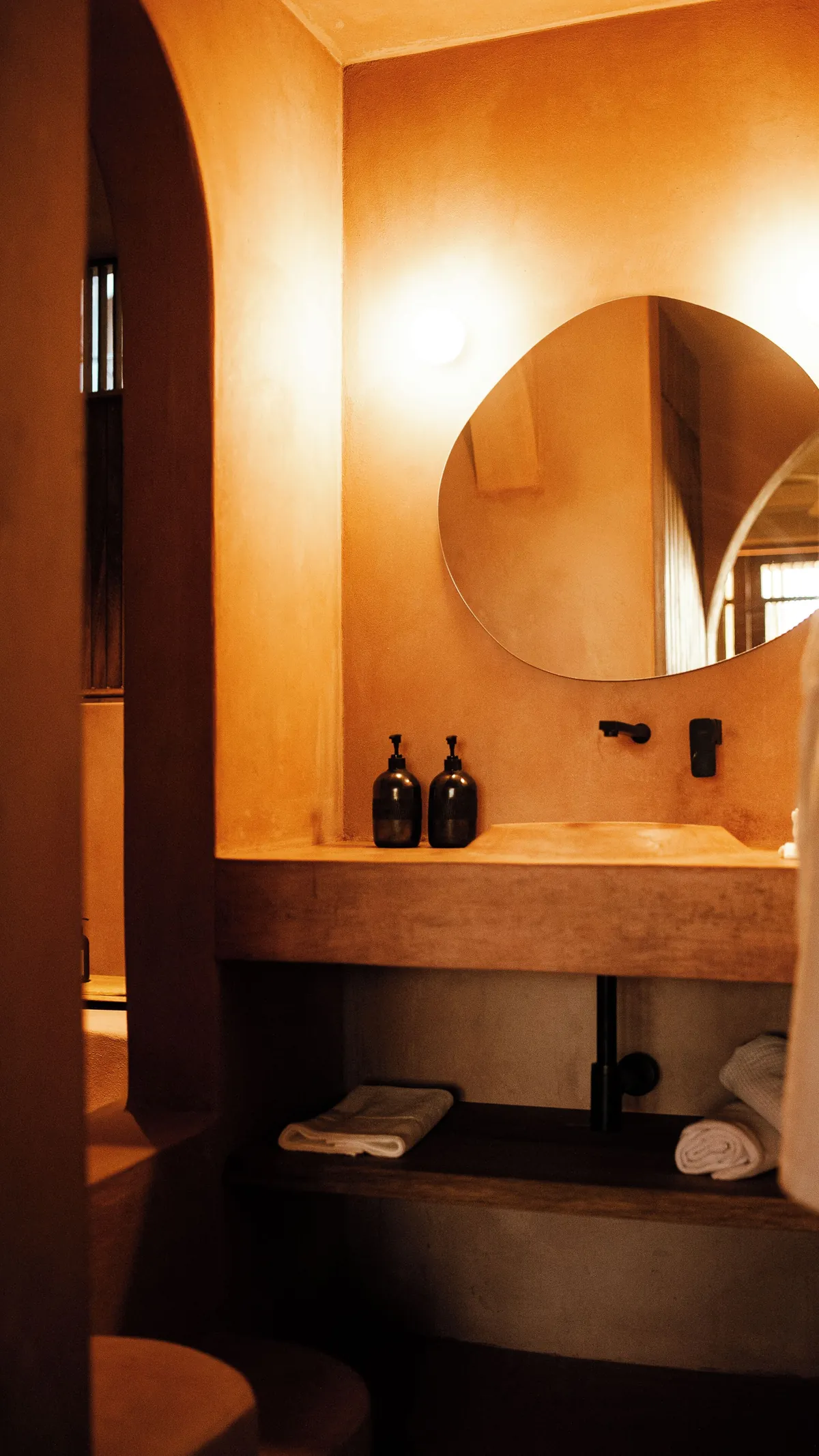 Grand Signature: lavabo de chukum con espejo de forma orgánica, repisa con toallas y amenidades